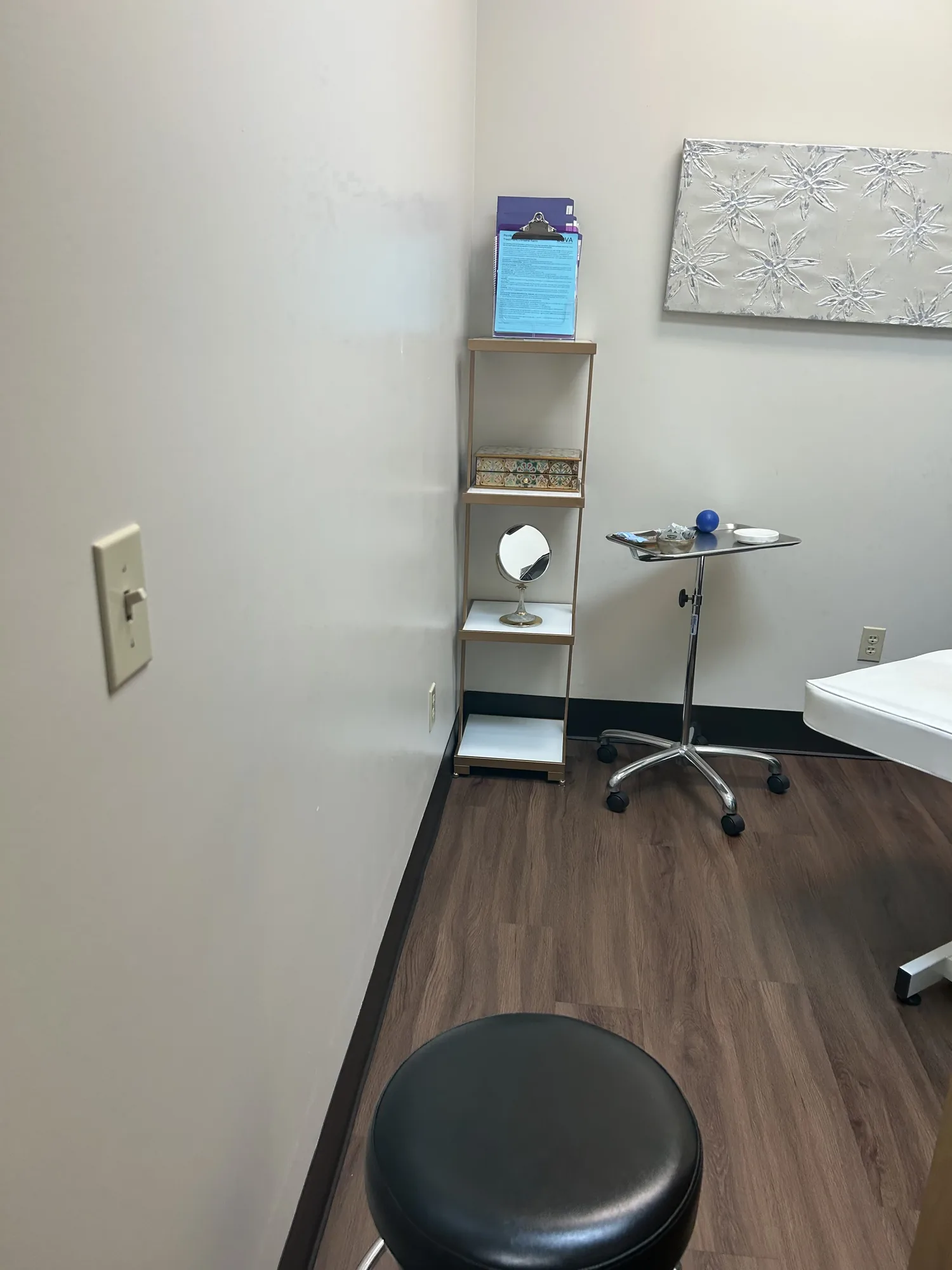 A corner of a treatment room with an instrument tray, shelving and stool